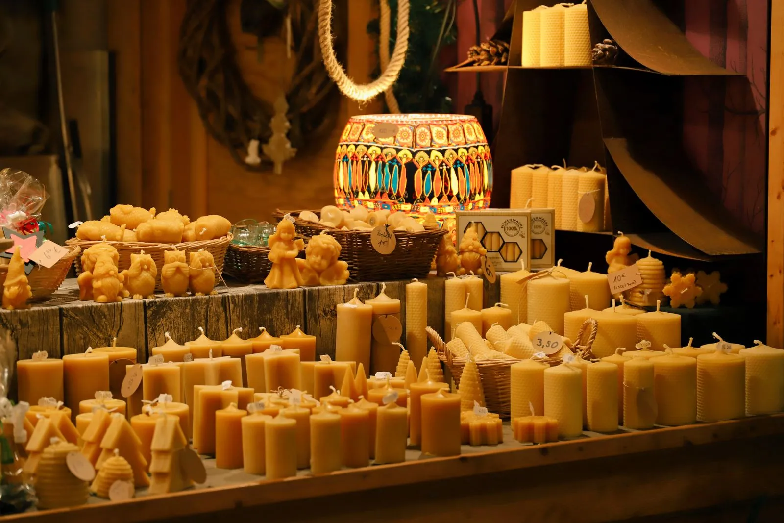 A wooden market table crowded with beeswax candles of every shape